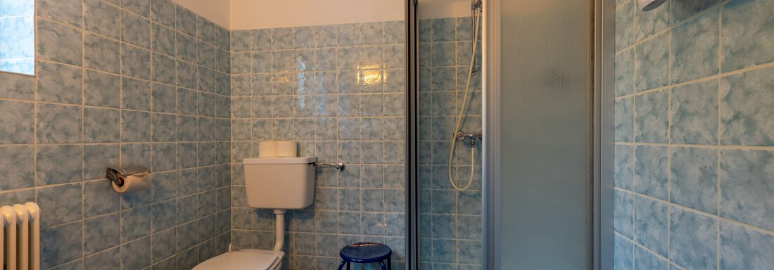 A small bathroom with blue tiles. It features a shower, a toilet, and a sink. - Appartementhaus Karlinger - Sölden