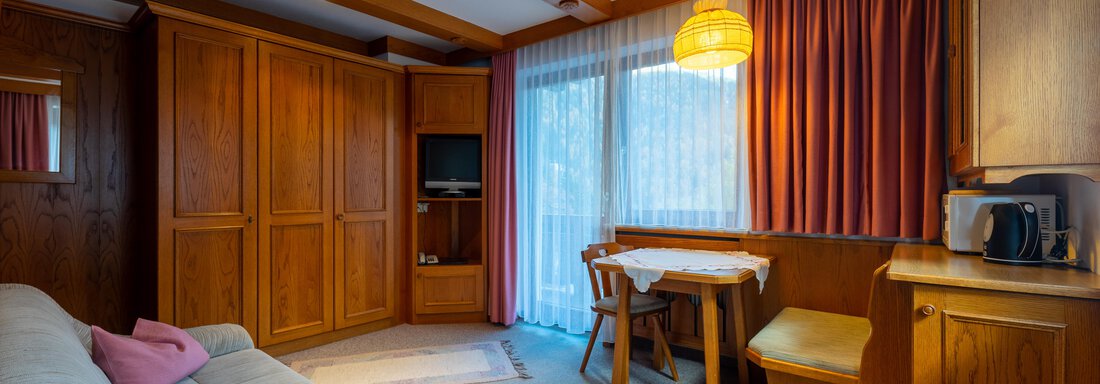 DSC00509-HDR A cozy living room with a white sofa and pink cushions. There is a table with chairs, a television, and large windows overlooking the outdoors. - Appartementhaus Karlinger - Sölden