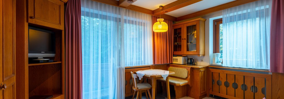 A cozy living space with wooden paneling and large windows. The room is bright and inviting, with a table and chairs as well as a couch. - Appartementhaus Karlinger - Sölden