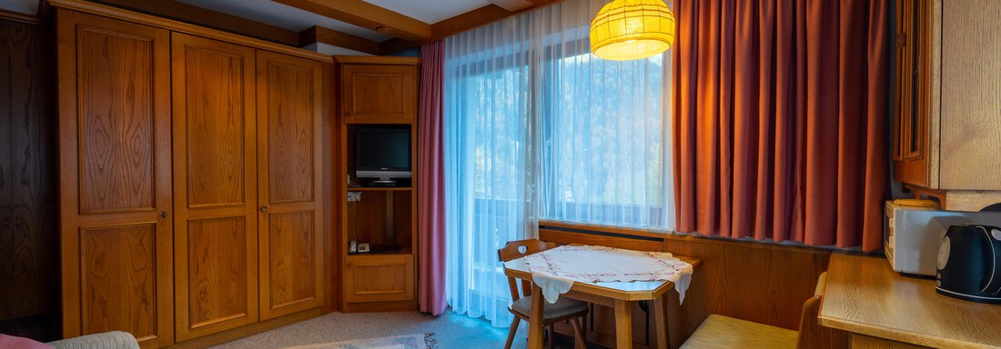 A cozy room with wooden paneling and a small table. Natural light streams into the room through the window. - Appartementhaus Karlinger - Sölden