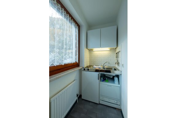 A small kitchen with a window through which light streams. There is a sink and some kitchen cabinets. - Appartementhaus Karlinger - Sölden