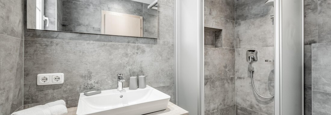 A modern bathroom with gray walls and a shower. On the sink shelf, there are two glasses and towels. - Appartementhaus Kathrin - Sölden