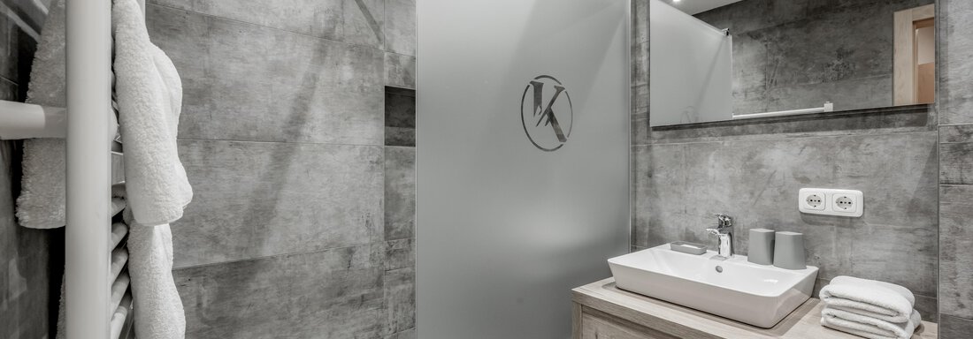 A modern bathroom with a shower cabin and grey walls. On the washbasin, there is a fresh towel and a bowl. - Appartementhaus Kathrin - Sölden