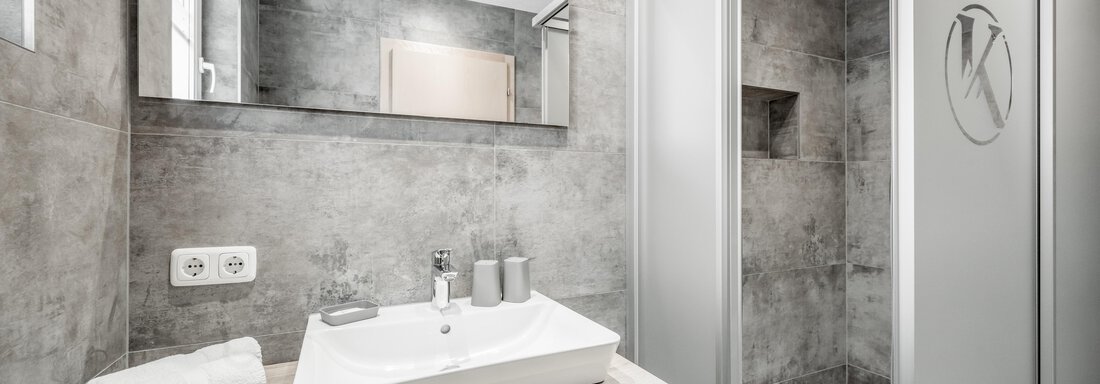 A modern bathroom with an elegant shower and a bright sink. The walls are kept in neutral gray tones, creating a calm atmosphere. - Appartementhaus Kathrin - Sölden