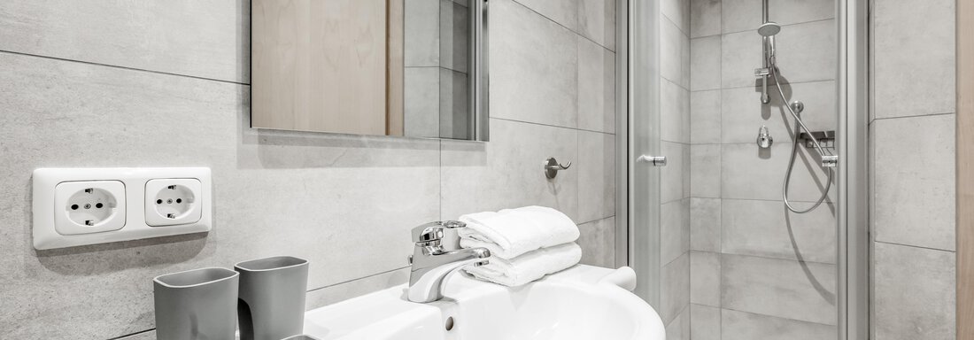A modern bathroom with gray tiles and a shower cabin. There is a sink with towels and two cups on the table. - Appartementhaus Kathrin - Sölden