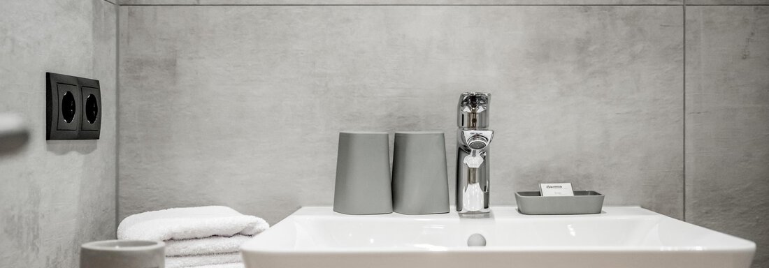 A modern bathroom with a white sink and gray walls. Towels and toiletries are neatly arranged. - Appartementhaus Kathrin - Sölden