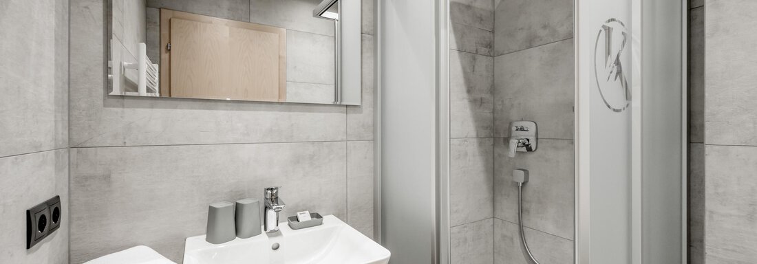 A modern bathroom with a shower and a sink. The walls are in a light gray color, and there are stylish accessories. - Appartementhaus Kathrin - Sölden