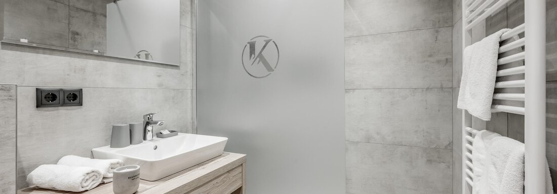 A modern bathroom with gray walls and an elegant shower enclosure. It features a wooden sink and towels that are neatly organized. - Appartementhaus Kathrin - Sölden