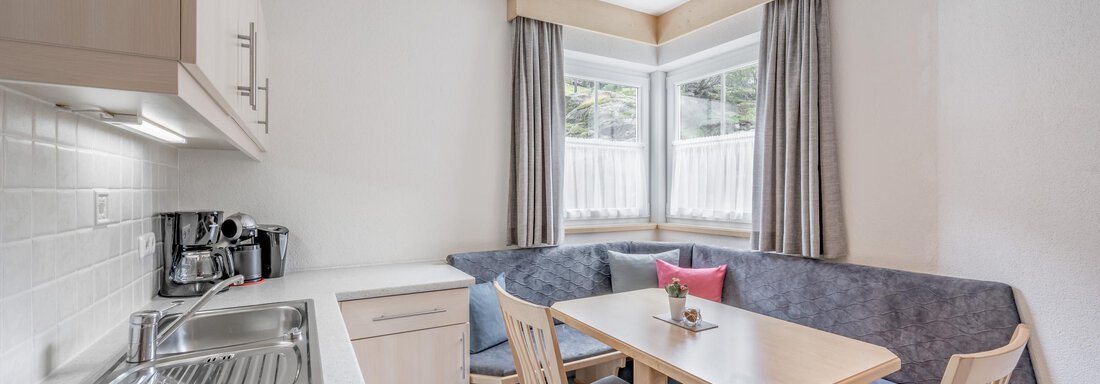 A bright, modern kitchen with a dining area. The table is equipped with chairs and a cozy bench. - Appartementhaus Kathrin - Sölden