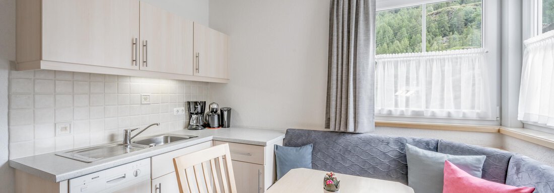 A modern kitchen with bright wooden cabinets and a dining table. Large windows provide plenty of daylight. - Appartementhaus Kathrin - Sölden