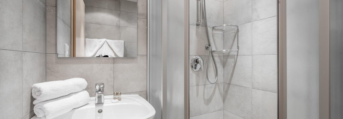 A modern bathroom with a shower and a sink. The walls are decorated with gray tiles, and fresh towels are ready. - Appartementhaus Kathrin - Sölden