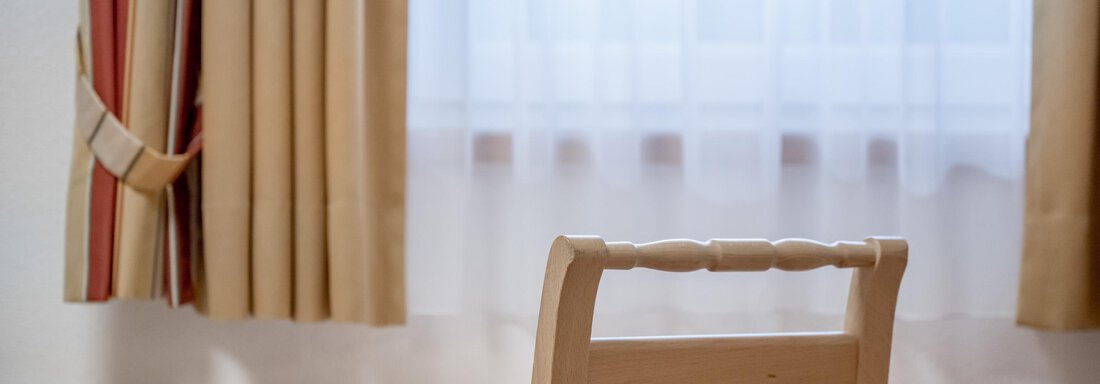 A simple room with a bright table, a chair, and curtains. Soft light flows in through the window. - Appartementhaus Kathrin - Sölden