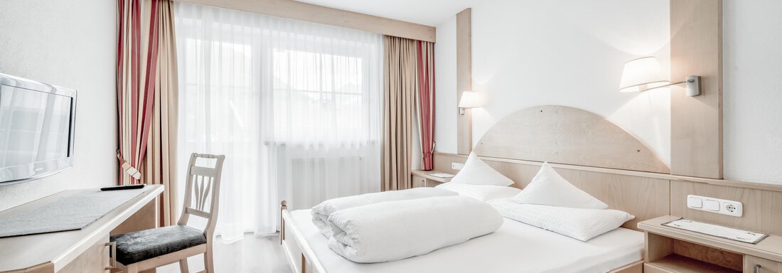 A modern room with a double bed and a desk. Large windows provide plenty of daylight. - Appartementhaus Kathrin - Sölden