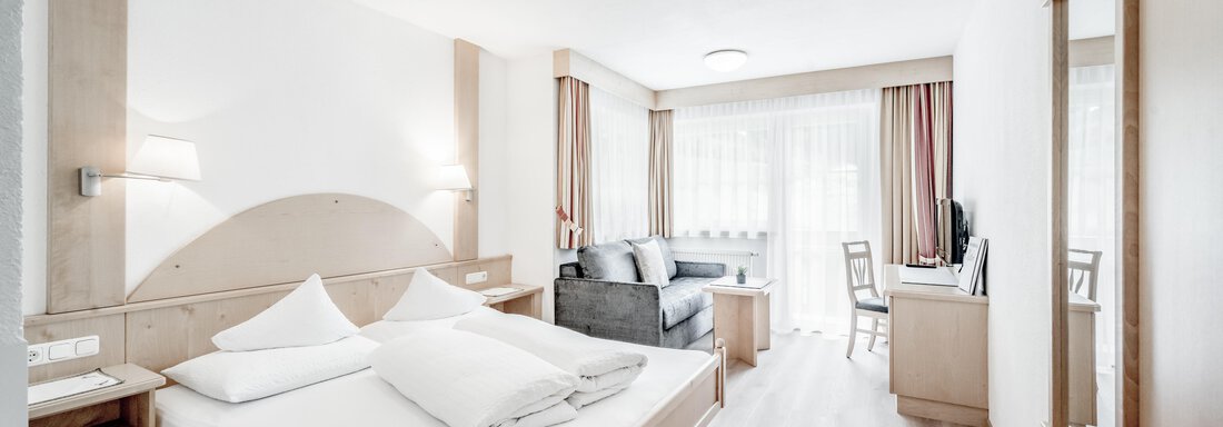 double room comfort ( 2-3) | © Kathrin Scheiber, Stephanie Lohmann (CC BY) A modern room with a double bed, a sofa, and a desk. Large windows let in plenty of daylight. - Appartementhaus Kathrin - Sölden