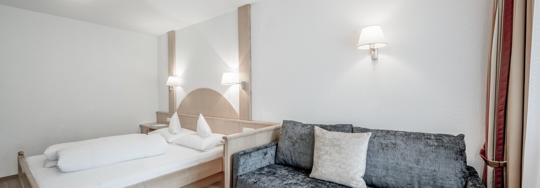 An elegant bedroom with a wooden bed and a sofa. The walls are light, and the lighting creates a cozy atmosphere. - Appartementhaus Kathrin - Sölden