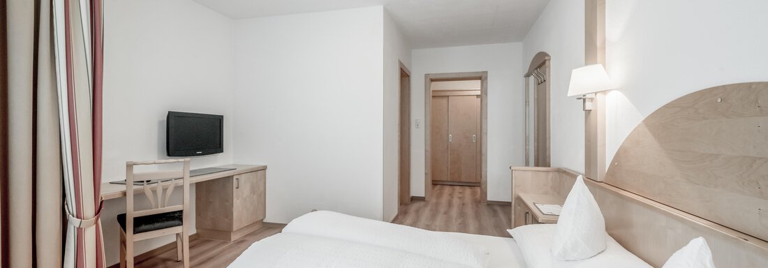 A modern hotel room with two beds and a cozy atmosphere. The room is minimally furnished, with a desk and a television. - Appartementhaus Kathrin - Sölden