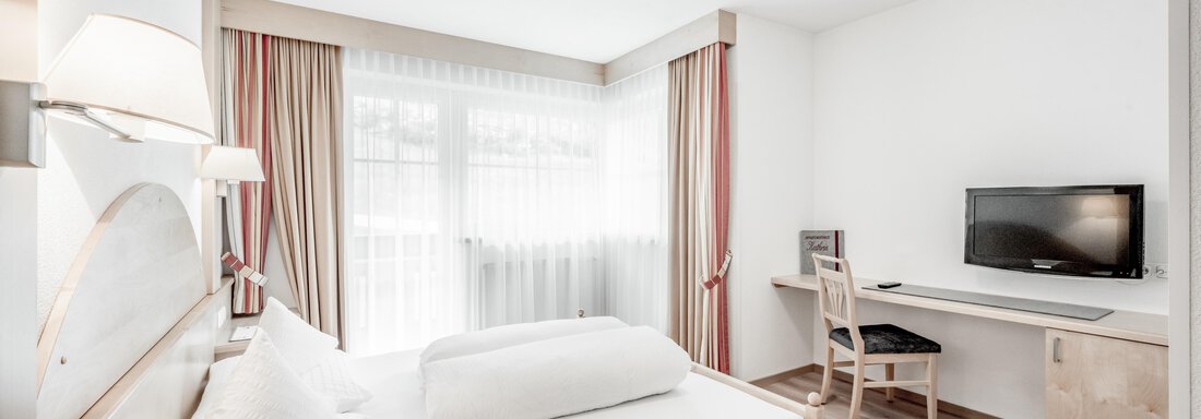 A modern bedroom with a double bed and a bright color scheme. There is a desk and a television on the wall. - Appartementhaus Kathrin - Sölden