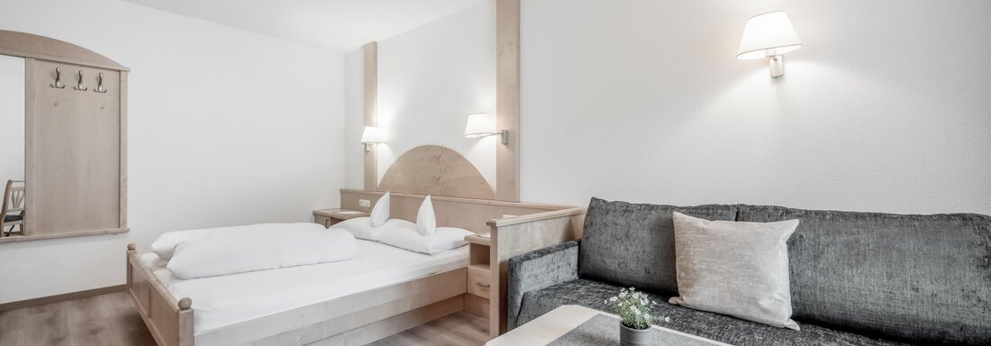 A modern bedroom with a double bed and a cozy couch. There is soft lighting and a small table with a plant. - Appartementhaus Kathrin - Sölden