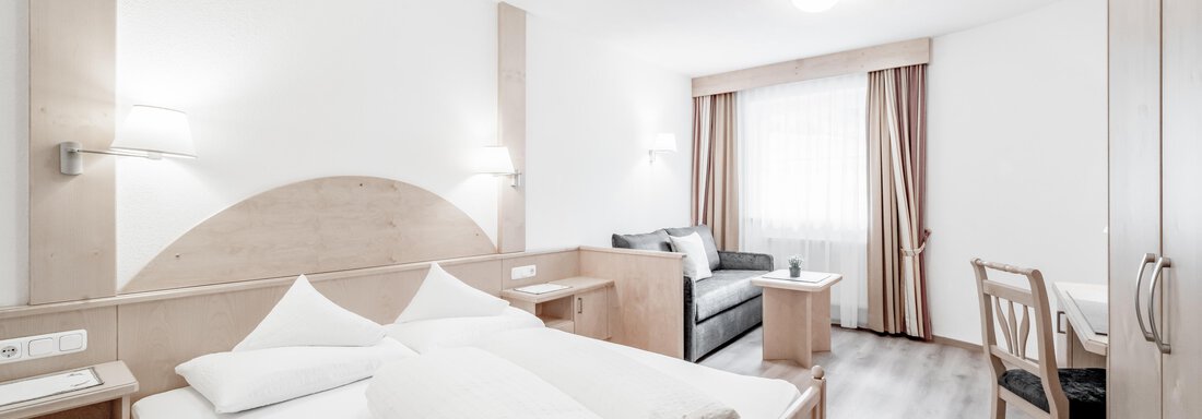 DSC_5095 A modern bedroom with a double bed and wood paneling. The room is bright and friendly, with a sofa and a desk. - Appartementhaus Kathrin - Sölden