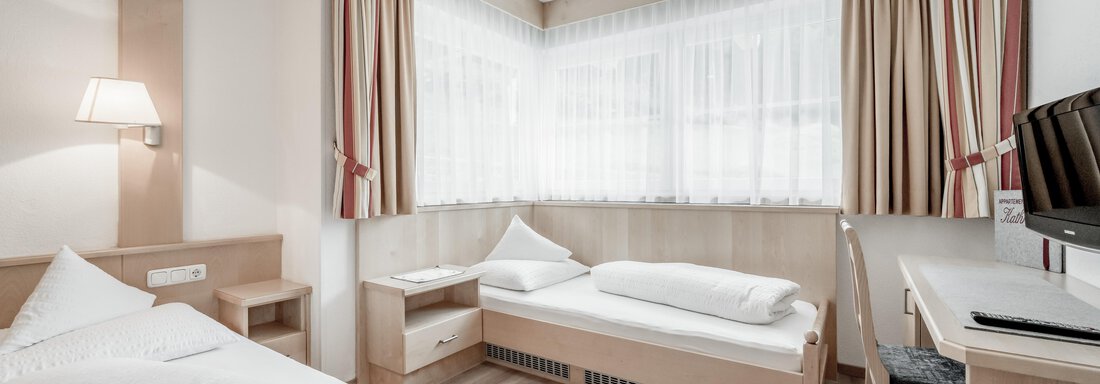 A simple room with two beds and a desk. The large window front provides plenty of daylight. - Appartementhaus Kathrin - Sölden