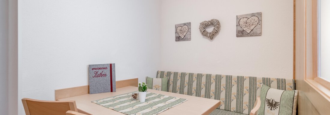 A cozy dining area with a table and wooden stools. The walls are plain white, and there are decorative pictures with heart motifs. - Appartementhaus Kathrin - Sölden