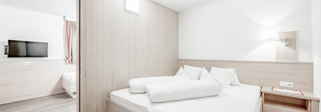 Economy Schlafzimmer A modern bedroom with a large bed and bright wooden interior. The walls are kept neutral and there is a television in the background. - Appartementhaus Kathrin - Sölden