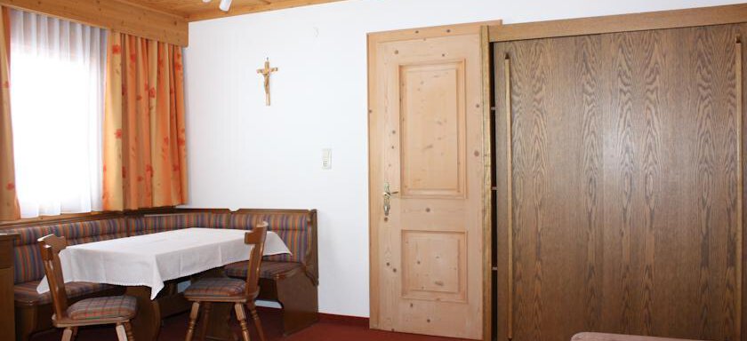 28388983 A cozy room with a table and chairs, as well as a cupboard. The walls are light and the curtains are orange. - Appt. Magda - Sölden