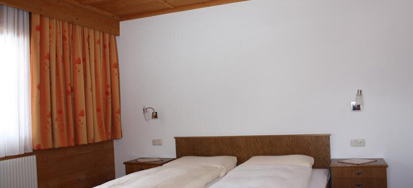 A simple bedroom with two single beds, wooden ceilings, and orange curtains. The room feels bright and inviting. - Appt. Magda - Sölden