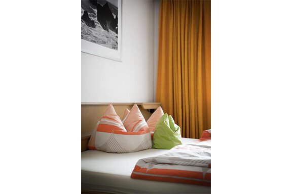 Schlafzimmer | © Appt. Schnöller (CC C) A cozy bedroom with colorful pillows on a bed. The curtains are in a warm shade of yellow. - Appt. Schnöller - Sölden