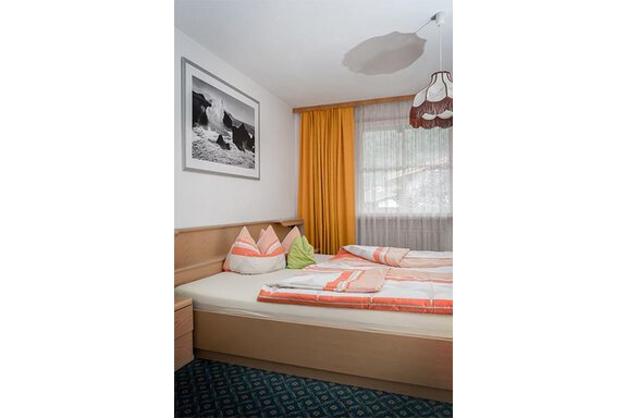 A cozy bedroom with a large bed and colorful pillows. The walls are decorated with a picture and curtains in warm colors. - Appt. Schnöller - Sölden
