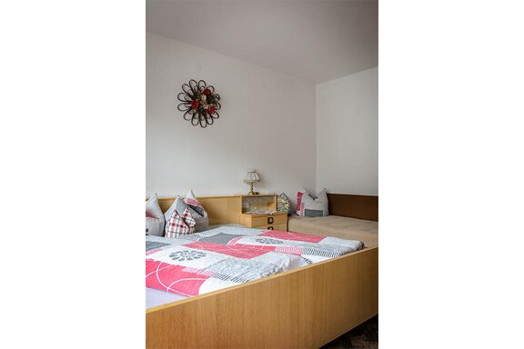 A simple bedroom with a large bed and several pillows. A decorative wall flower hangs on the wall, and a bedside table with a lamp stands next to it. - Appt. Schnöller - Sölden