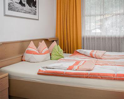 A cozy bedroom with a double bed and colorful cushions. The windows are decorated with curtains in warm colors. - Appt. Schnöller - Sölden