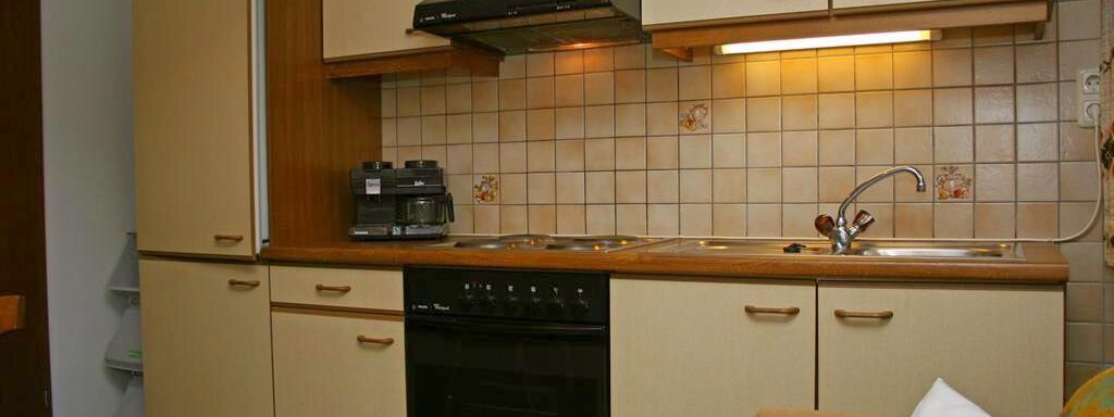 A modern kitchen with wooden fronts and matching cabinets. It features a stove, a refrigerator, and a sink. - Appt. Schnöller - Sölden