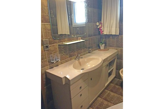 A modern bathroom with a sink and mirror. There are bright tiles and a windowsill with a plant. - Appt. Schnöller - Sölden