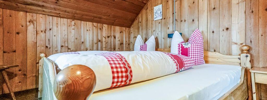 A cozy bedroom with wood paneling and two beds. The bedding has a red and white checkered pattern and there are pillows with a decorative touch. - Arnold - Sölden