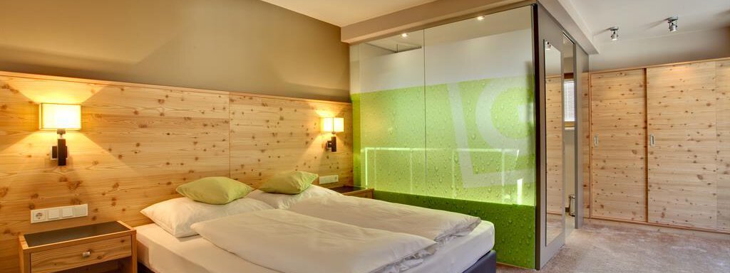 Ein modernes Schlafzimmer mit einem Doppelbett und Holzverkleidung. Der Raum hat eine große Glaswand, die einen Hauch von Grün zeigt. - Bäckelar Wirt - Sölden