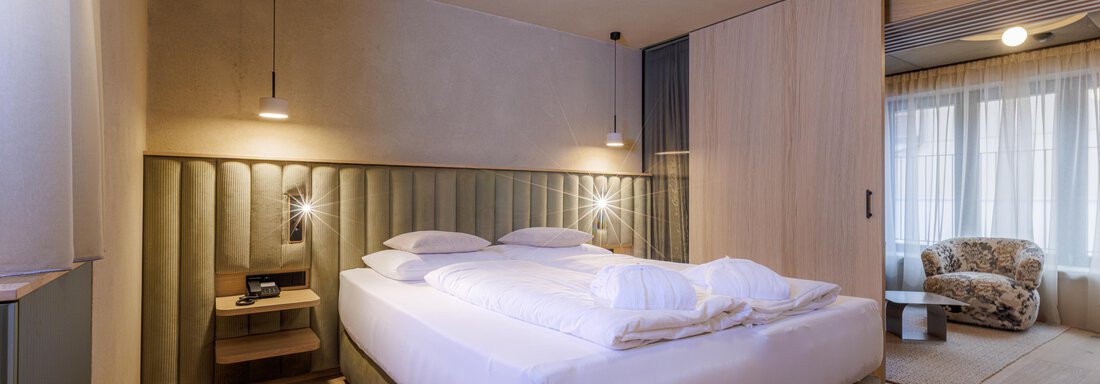Ein modernes Schlafzimmer mit einem großen Bett und stilvoller Beleuchtung. Die ruhigen Farben und minimalistischen Möbel schaffen eine entspannte Atmosphäre. - Bäckelar Wirt - Sölden