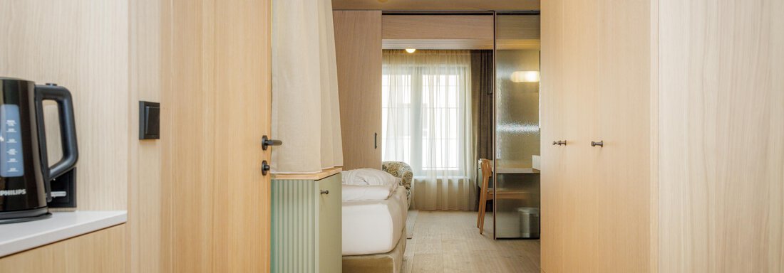 Ein moderner Hotelflur mit Holzverkleidung und einem Tageslichtfenster. Im Hintergrund ist ein gemütliches Schlafzimmer zu sehen. - Bäckelar Wirt - Sölden