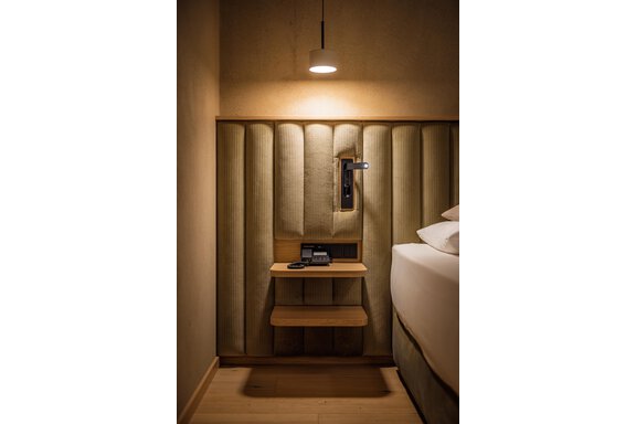Ein modernes Schlafzimmer mit einer stilvollen Wandverkleidung und einer schlichten Nachttischlampe. Der Nachttisch bietet Platz für ein Telefon und persönliche Gegenstände. - Bäckelar Wirt - Sölden