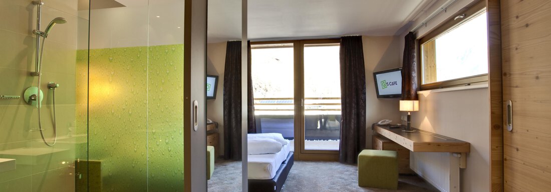 Ein modernes Hotelzimmer mit einem Badbereich und einer Dusche. Große Fenster lassen viel Licht herein und bieten einen Blick nach außen. - Bäckelar Wirt - Sölden