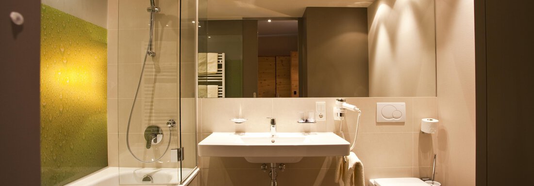 Ein modernes Badezimmer mit einer Dusche und einer Badewanne. Helle Beleuchtung und elegante Armaturen schaffen eine angenehme Atmosphäre. - Bäckelar Wirt - Sölden