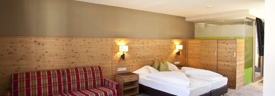 Ein komfortables Hotelzimmer mit einem Doppelbett und einer gemütlichen Sitzecke. Die Wände sind mit Holzvertäfelung und warmen Farben gestaltet. - Bäckelar Wirt - Sölden
