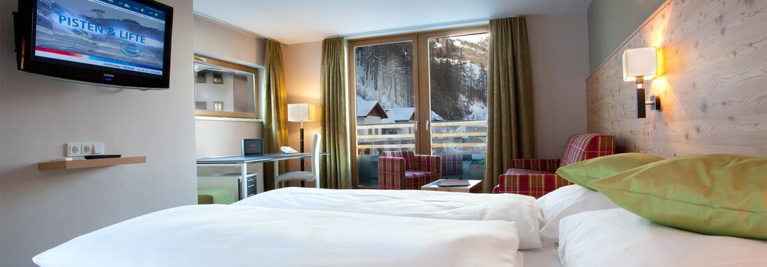 Ein modernes Hotelzimmer mit zwei Betten und einem Fernseher. Große Fenster bieten einen Blick auf die verschneite Landschaft. - Bäckelar Wirt - Sölden