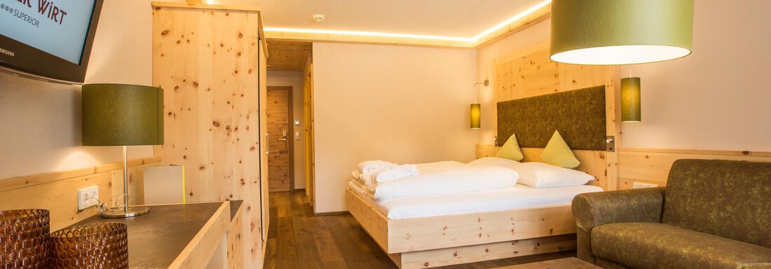 Ein modernes Hotelzimmer mit Holzmöbeln und warmen Farben. Es gibt ein Doppelbett, eine Couch und einen großen Fernseher. - Bäckelar Wirt - Sölden
