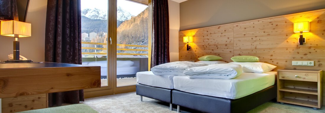 Ein modernes Hotelzimmer mit zwei Betten, Holzelementen und großen Fenstern. Der Raum hat eine gemütliche Atmosphäre und einen Blick auf die Berge. - Bäckelar Wirt - Sölden