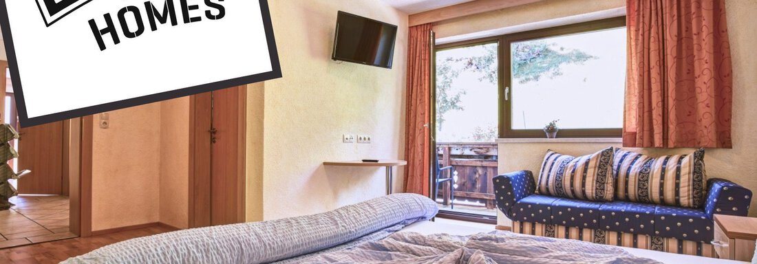 A cozy room with wooden flooring, a large window, and a lovely seating area. The bedding is neat, and an inviting view outside is visible. - Belledonne Ski in & out Appartements - Sölden
