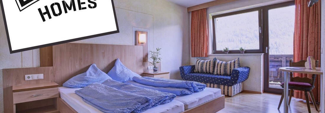 A cozy room with a large bed and a seating area. There is a balcony with an open view and plenty of daylight. - Belledonne Ski in & out Appartements - Sölden