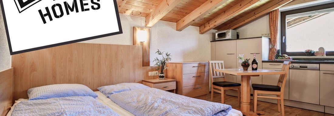 A cozy room with a double bed, wooden beam ceiling, and a small seating area. The decor is simple and modern, perfect for a stay. - Belledonne Ski in & out Appartements - Sölden