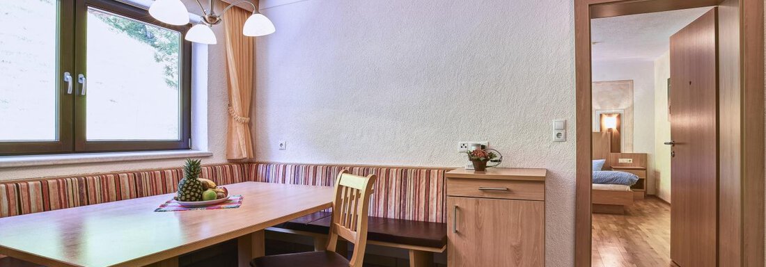 A cozy dining area with a wooden table and chairs. In the background, a bedroom can be seen. - Belledonne Ski in & out Appartements - Sölden