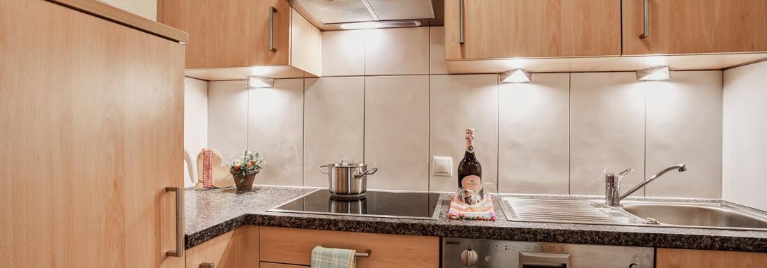 A modern kitchen with wooden cabinets and a dark workspace. Pots and a bottle of wine are on the countertop. - Belledonne Ski in & out Appartements - Sölden